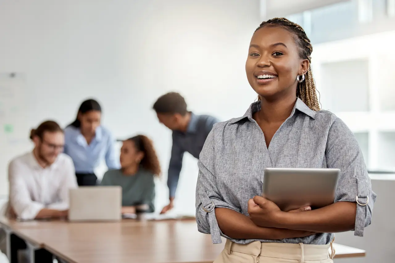 A imagem apresenta uma empresária negra e jovem segurando um tablet digital enquanto estava na sala de reuniões. O tema do artigo é empreendedorismo corporativo.